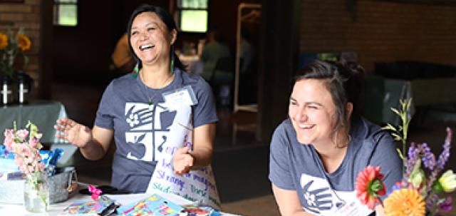 Two educators smile at check-in table at Farm to School Institute. They wear matching shirts.
